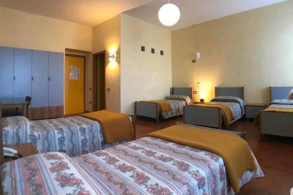 A hotel room with four beds, a wooden wardrobe, a desk, and a small table.