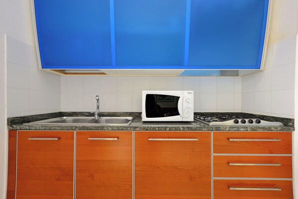 A kitchen with a microwave, stove, sink, and wooden cabinets. - Spacious and Comfy Flat With Balcony (Lignano Sabbiadoro)