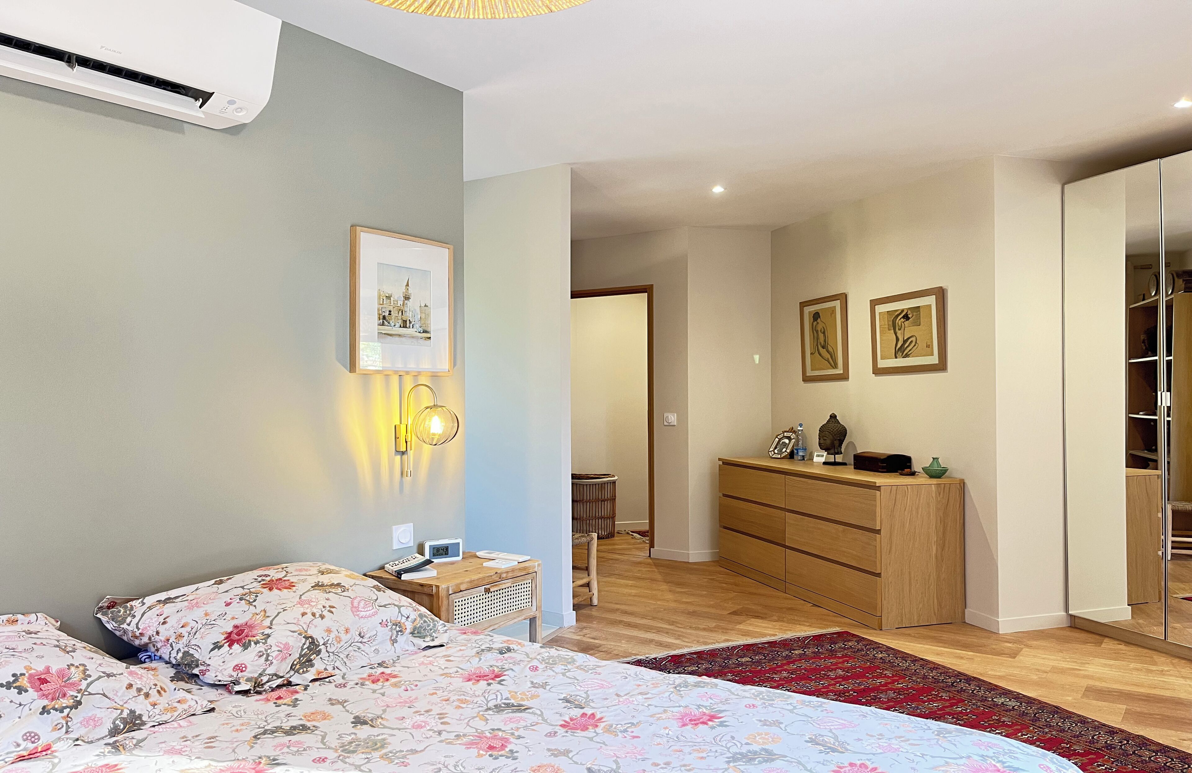 A bedroom with a bed, bedside table, wall-mounted lamp, and a dresser.