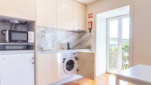 A compact kitchen with a microwave, a washing machine, and a sink. - Corticeira Living (Porto)