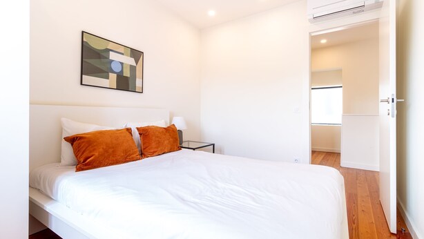 A bedroom with a bed, a nightstand, an air conditioning unit, and a door leading to another room. - Corticeira Living (Porto)