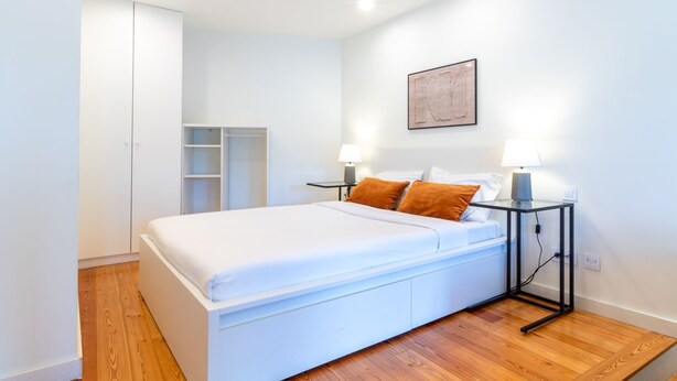 A modern bedroom with a single bed, white bedding, two bedside lamps, and a small bedside table. - Corticeira Living (Porto)