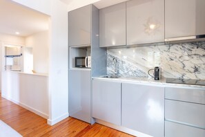 A modern kitchen with a marble countertop, built-in appliances, and a wooden floor. - Corticeira Living (Porto)
