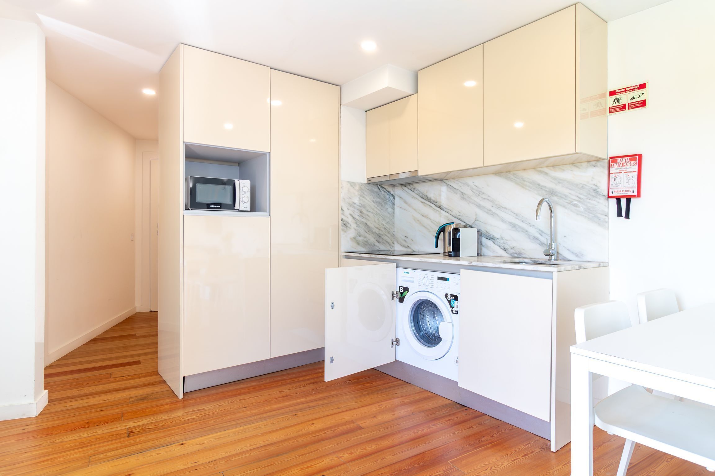 Una cuina compacta amb rentadora integrada, microones i un lavabo amb taulell de marbre.
