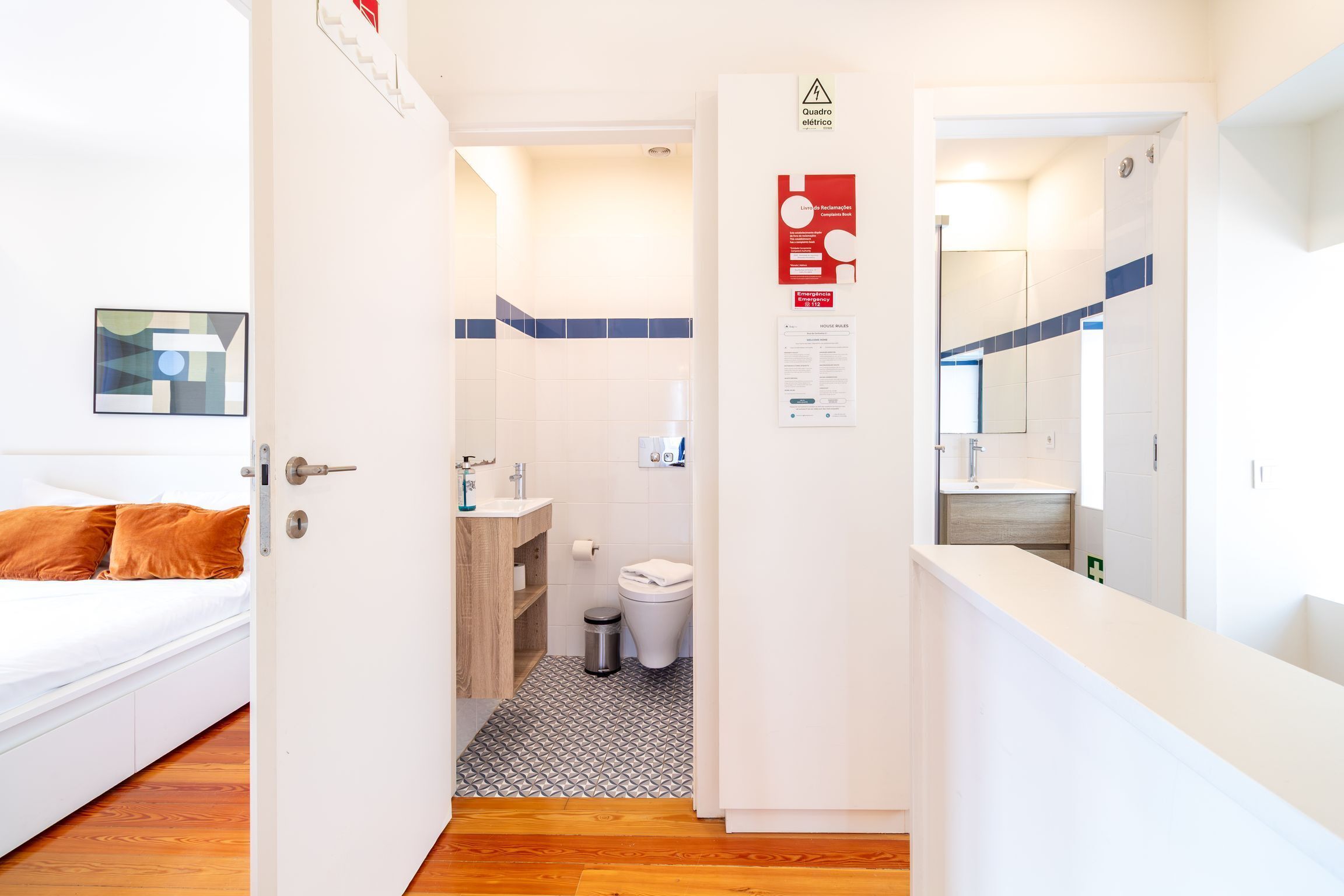 Habitación de hotel con cama, baño con inodoro, lavamanos y ducha, y un pasillo que conduce a otra habitación.