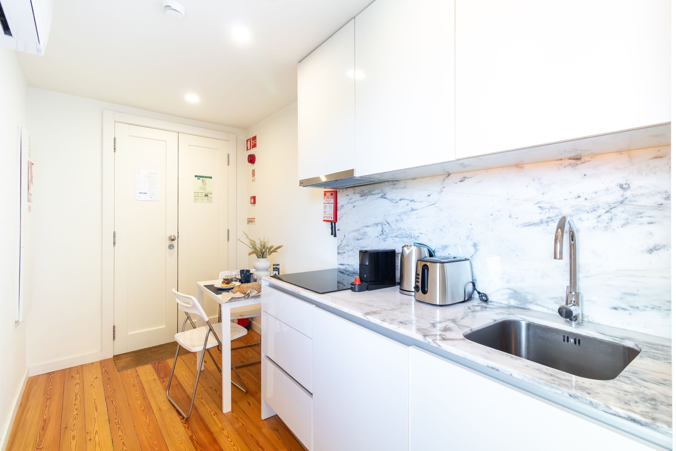 Cocina compacta con encimera de mármol, lavamanos de acero inoxidable y electrodomésticos modernos.