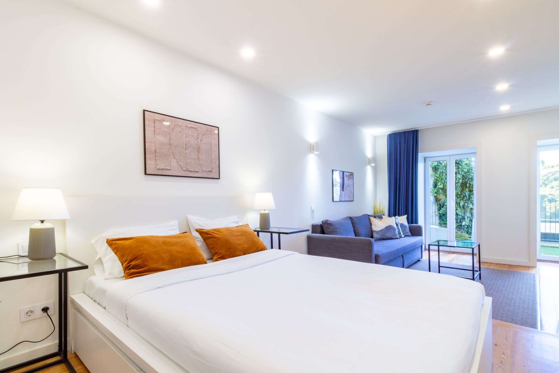 A hotel room with a large bed, bedside lamps, a sofa, and a view of the outdoors.