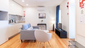 A modern living room with a grey sofa, a round white chair, a small table, and a TV. - Corticeira Living (Porto)