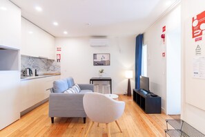 A modern living room with a grey sofa, a round white chair, a small table, and a TV. - Corticeira Living (Porto)