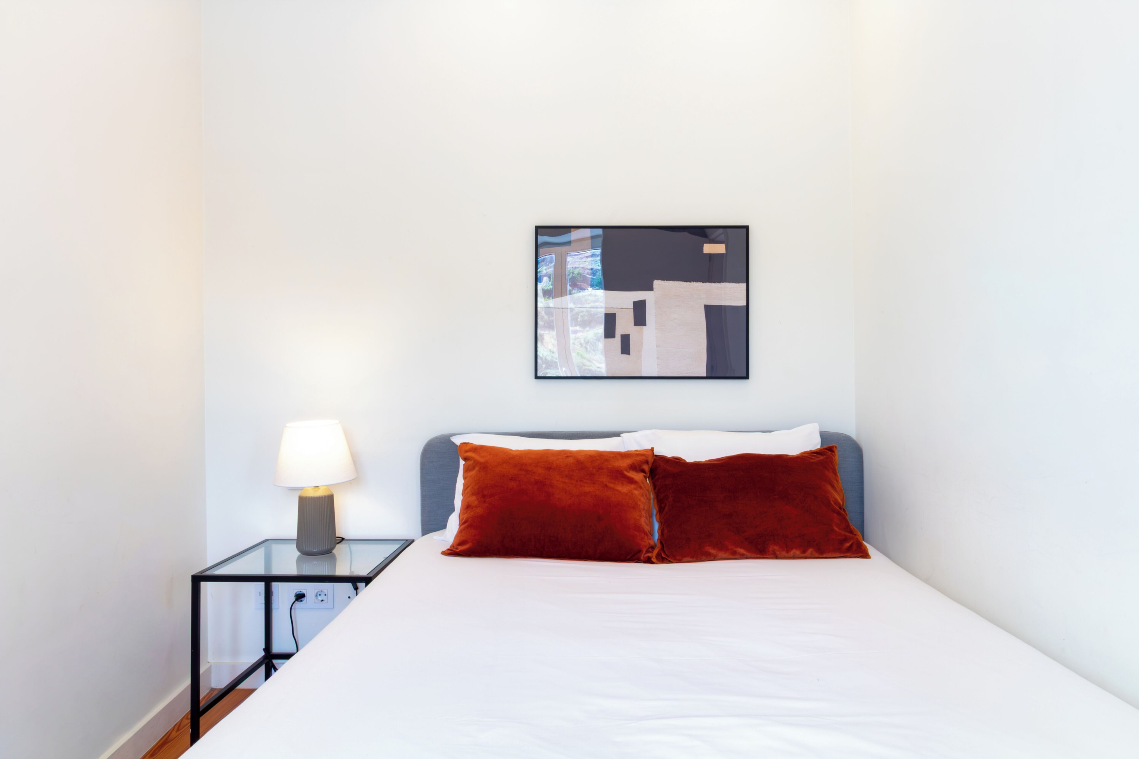 Una camera d'albergo con un letto, un comodino, una lampada e un'opera d'arte astratta appesa al muro.