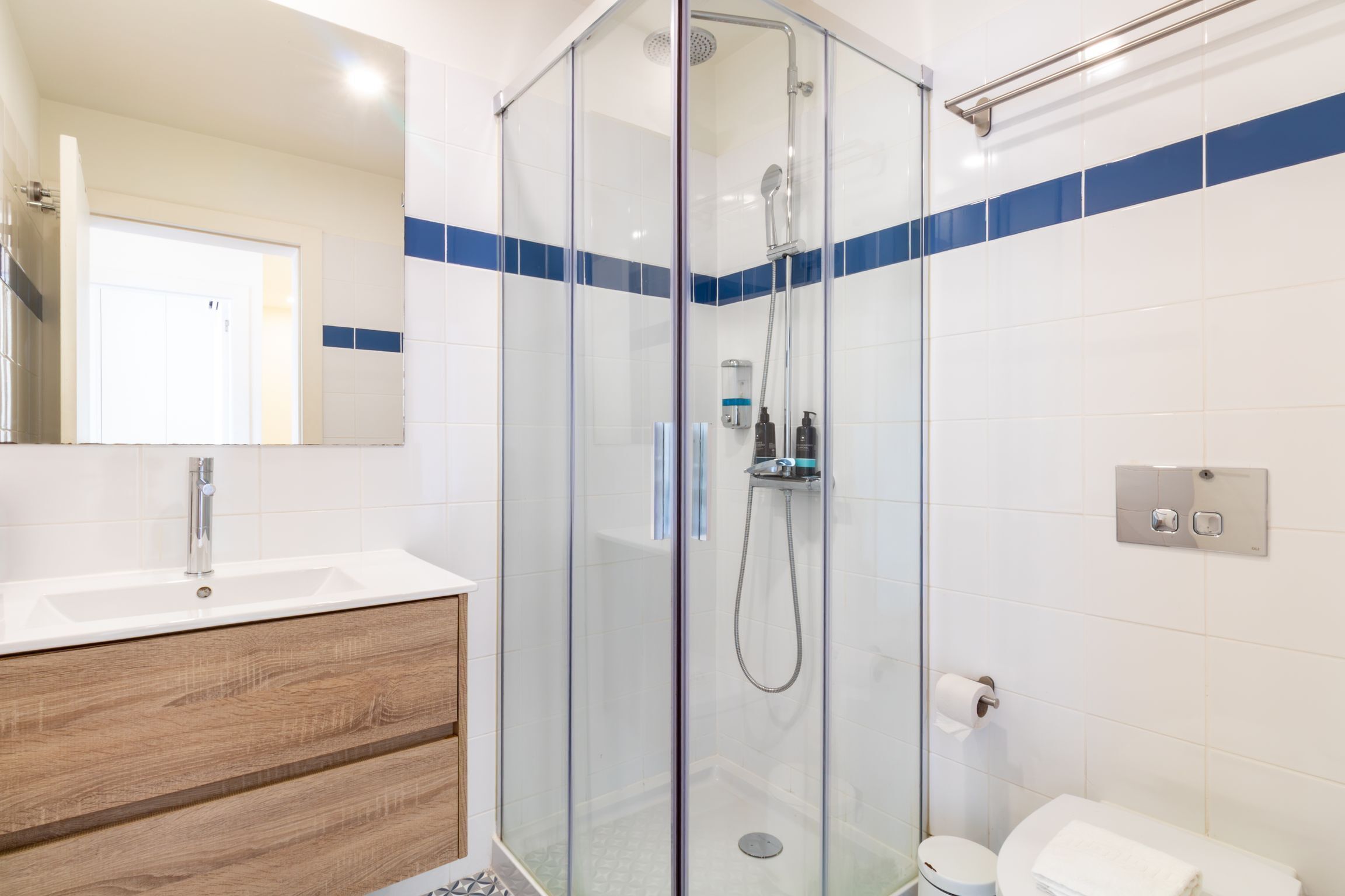 Een moderne badkamer met een douche met glazen wand, een houten wastafelmeubel en een wit toilet.