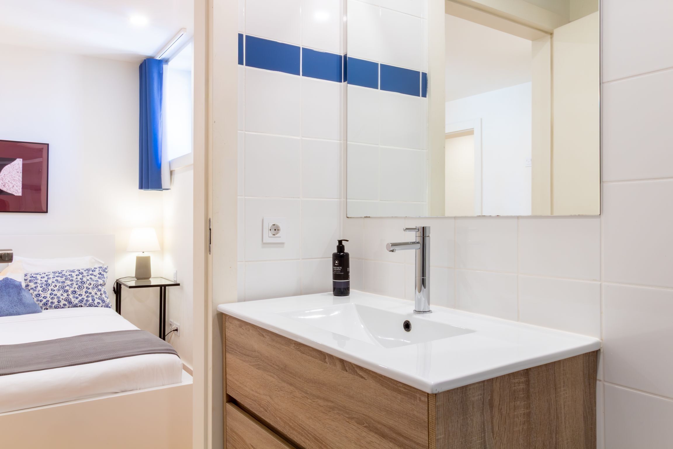 Une chambre d’hôtel comprenant un lit, une table de chevet avec une lampe, un miroir et une salle de bain avec un lavabo et un miroir.