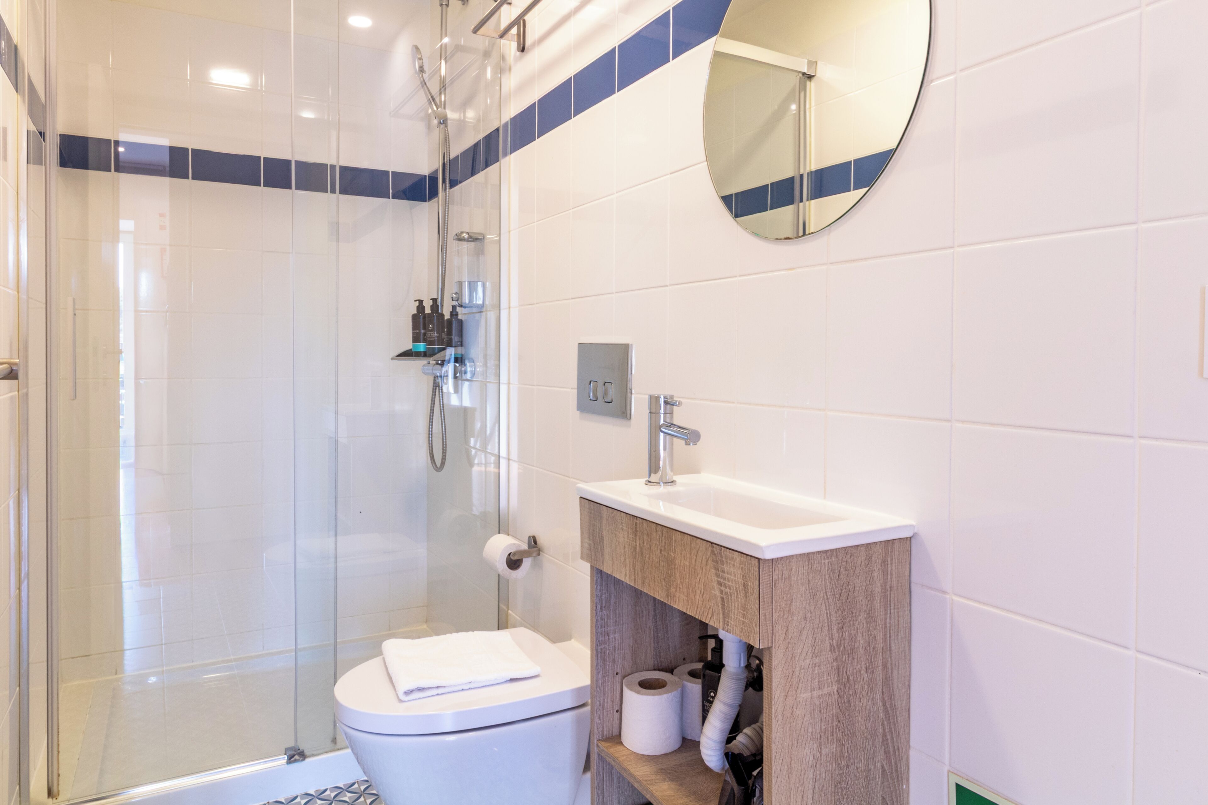 A modern bathroom with a glass shower enclosure, a white toilet, and a wooden vanity with a sink.