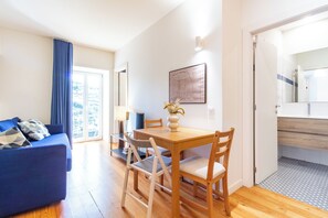 A modern living room with a blue sofa, a wooden dining table, and a large window. - Corticeira Living (Porto)