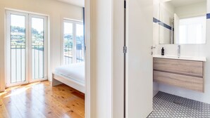 A modern bedroom with a large window, a balcony, and a bathroom with a mirror and sink. - Corticeira Living (Porto)