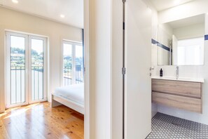 A modern bedroom with a large window, a balcony, and a bathroom with a mirror and sink. - Corticeira Living (Porto)