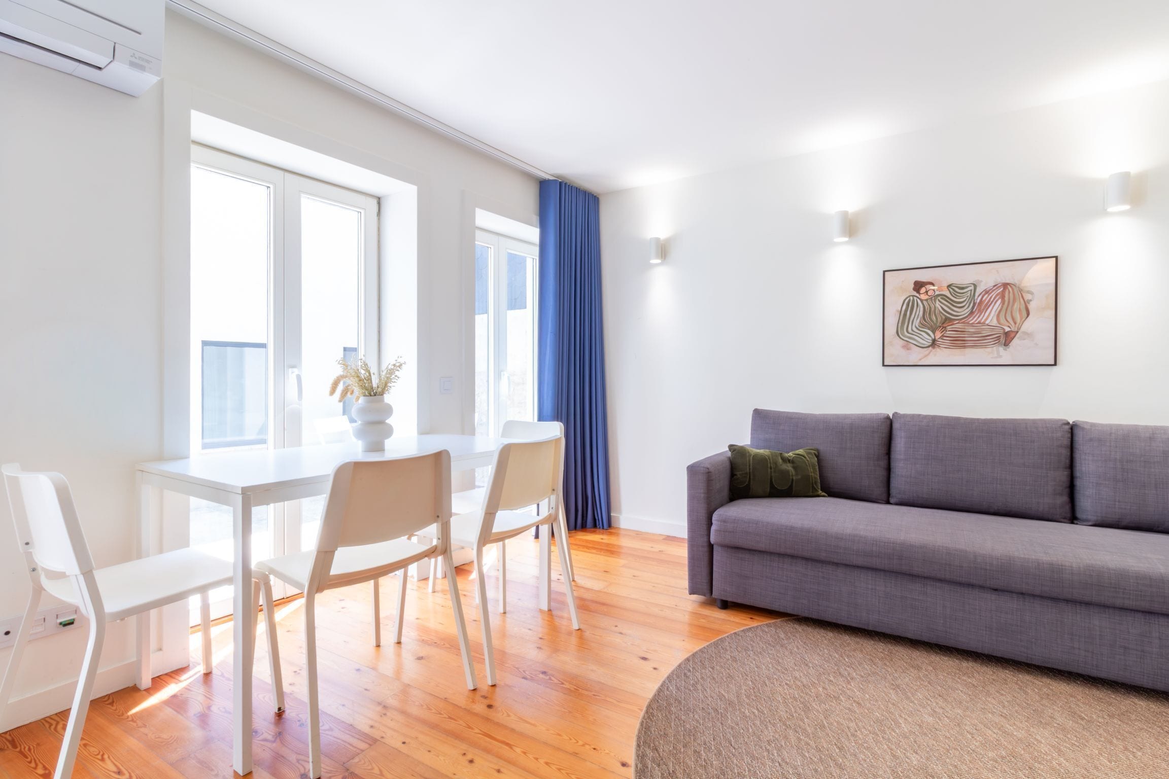 Un salon moderne avec un canapé gris, des chaises blanches et une table à manger.