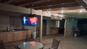 A kitchen with wooden cabinets, a dining table with chairs, a ceiling fan, and a TV displaying a show. - Desert Sunshine Lagoon, Beautiful 2 bed 2 bath house with pool and amazing patio (Yuma)