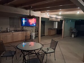 A kitchen with wooden cabinets, a dining table with chairs, a ceiling fan, and a TV displaying a show.