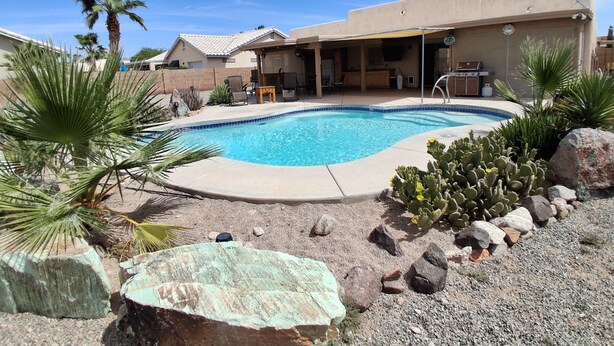 A swimming pool with a patio area, surrounded by desert plants and rocks. - Desert Sunshine Lagoon, Beautiful 2 bed 2 bath house with pool and amazing patio (Yuma)