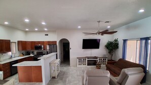 A modern kitchen with a central island, a dining area with a sofa, and a flat-screen TV mounted on the wall. - Desert Sunshine Lagoon, Beautiful 2 bed 2 bath house with pool and amazing patio (Yuma)