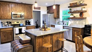 A kitchen with wooden cabinets, a central island with stools, a microwave, stove, and a refrigerator. - Lakefront!  Fire Pit, Kayaks, Foosball, Sparkling Clean Hot Tub (Granbury)