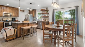 A kitchen with wooden cabinets, a central island, bar stools, a dining table with chairs, and pendant lighting. - Lakefront!  Fire Pit, Kayaks, Foosball, Sparkling Clean Hot Tub (Granbury)