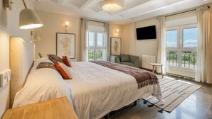 A bedroom with a large bed, bedside lamps, a flat-screen TV, a view of the outdoors, and a small table.