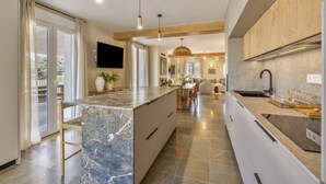A modern kitchen with a marble island, wooden cabinets, and a large window.