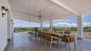 A covered patio with a dining table and chairs, a railing, and a view of the landscape.