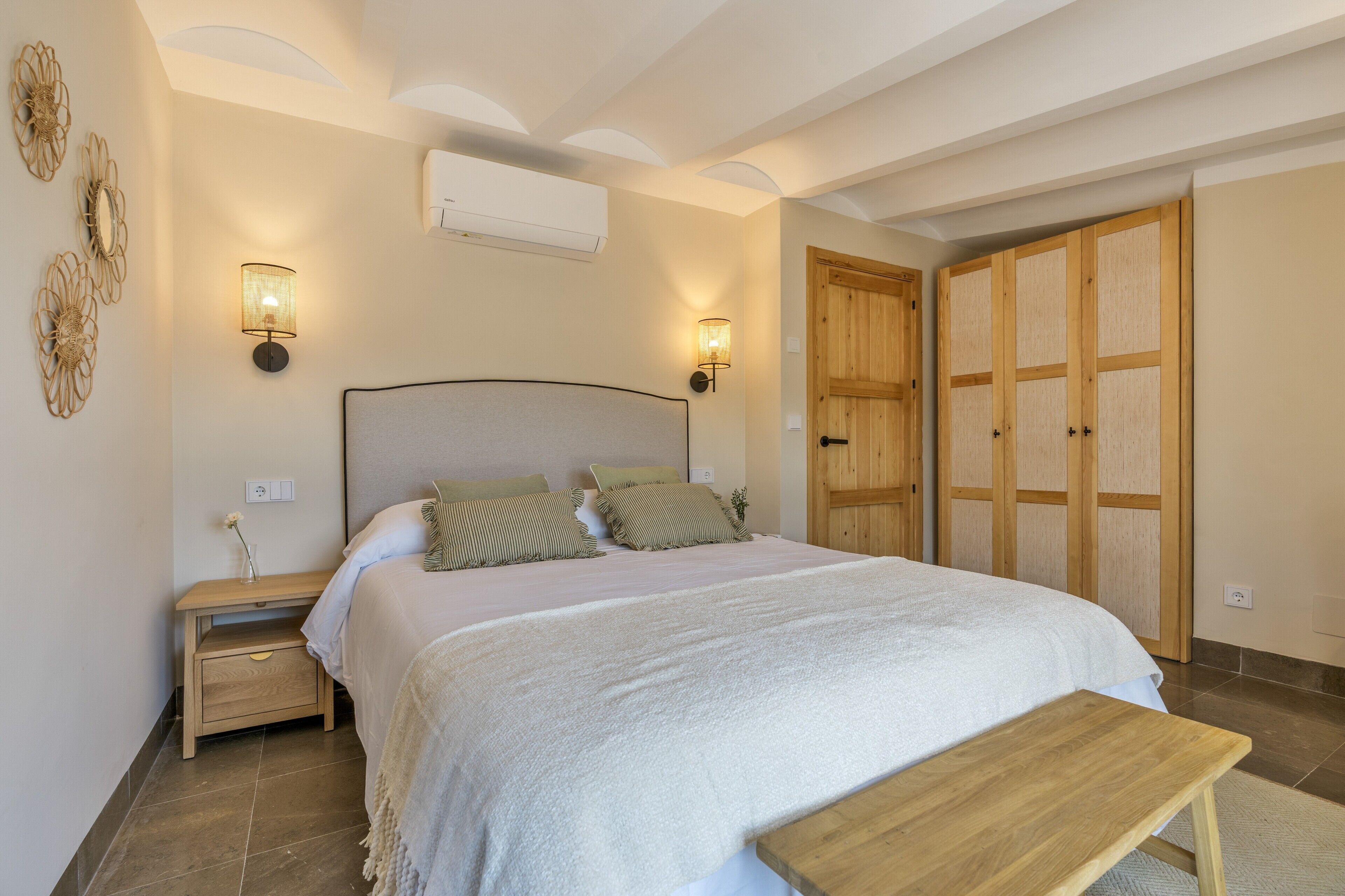 A bedroom with a bed, bedside tables, wall-mounted lamps, an air conditioner, and a wooden wardrobe.