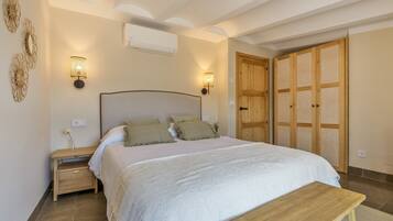 A bedroom with a bed, bedside tables, wall-mounted lamps, an air conditioner, and a wooden wardrobe.