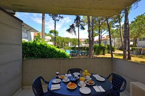 A covered patio with a table set for breakfast, including plates, cups, and a kettle. - Bright Apartment With Balcony (Lignano Sabbiadoro)