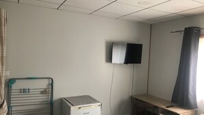A room with a desk, a television mounted on the wall, a radiator, and a small white appliance.