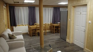 A room with a wooden floor, a sofa, a dining table with chairs, a refrigerator, and a door.