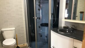A bathroom with a toilet, a glass-enclosed shower, and a sink with a mirror.