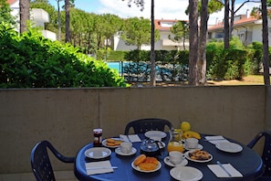 Ein runder Tisch mit Frühstücksangebot, Stühlen und Blick auf einen Swimmingpool und Gebäude.