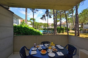 Une terrasse couverte avec une table mise pour le petit-déjeuner, comprenant des assiettes, des tasses et une bouilloire.