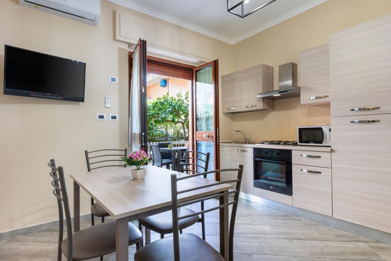 A modern kitchen with a dining area, built-in appliances, and a TV mounted on the wall.