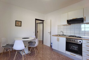 A compact kitchen with a gas stove, oven, and white cabinets. There is a small dining table with chairs.
