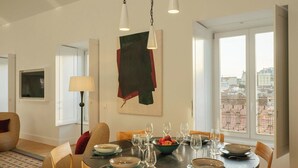 A dining area with a round table, chairs, and a view of the city through large windows. - Ando Living - Fanqueiros House (Lisbon)