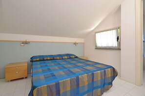 A bedroom with a bed, a nightstand, a window with curtains, and a door. - Comfort Getaway Apartment With Pool (Lignano Sabbiadoro)