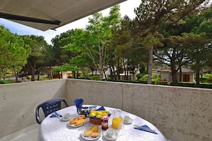 A balcony with a table set for breakfast, including bread, pastries, fruit, and beverages. - Peaceful Stay in Lignano Pineta (Lignano Sabbiadoro)