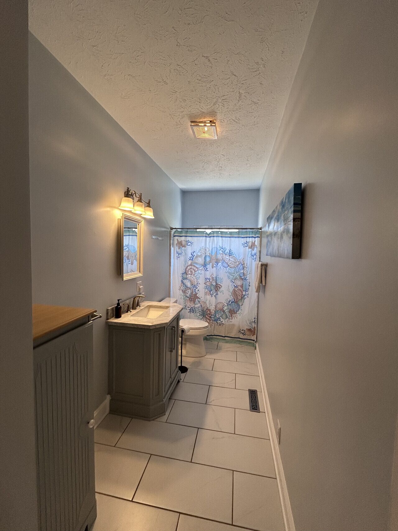 Un bagno con doppio lavabo, un water, una tenda da doccia a tema marino e un lampadario al soffitto.