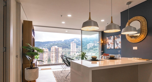 A modern kitchen with a large island, pendant lights, and a view of the city. - Apartamento Urban Studios (Medellín)