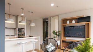 A modern kitchen with a dining area, a TV on a wooden shelf, and a potted plant. - Apartamento Urban Studios (Medellín)