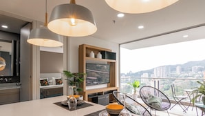 A modern kitchen with a large window, a dining area with chairs, and a view of a cityscape. - Apartamento Urban Studios (Medellín)