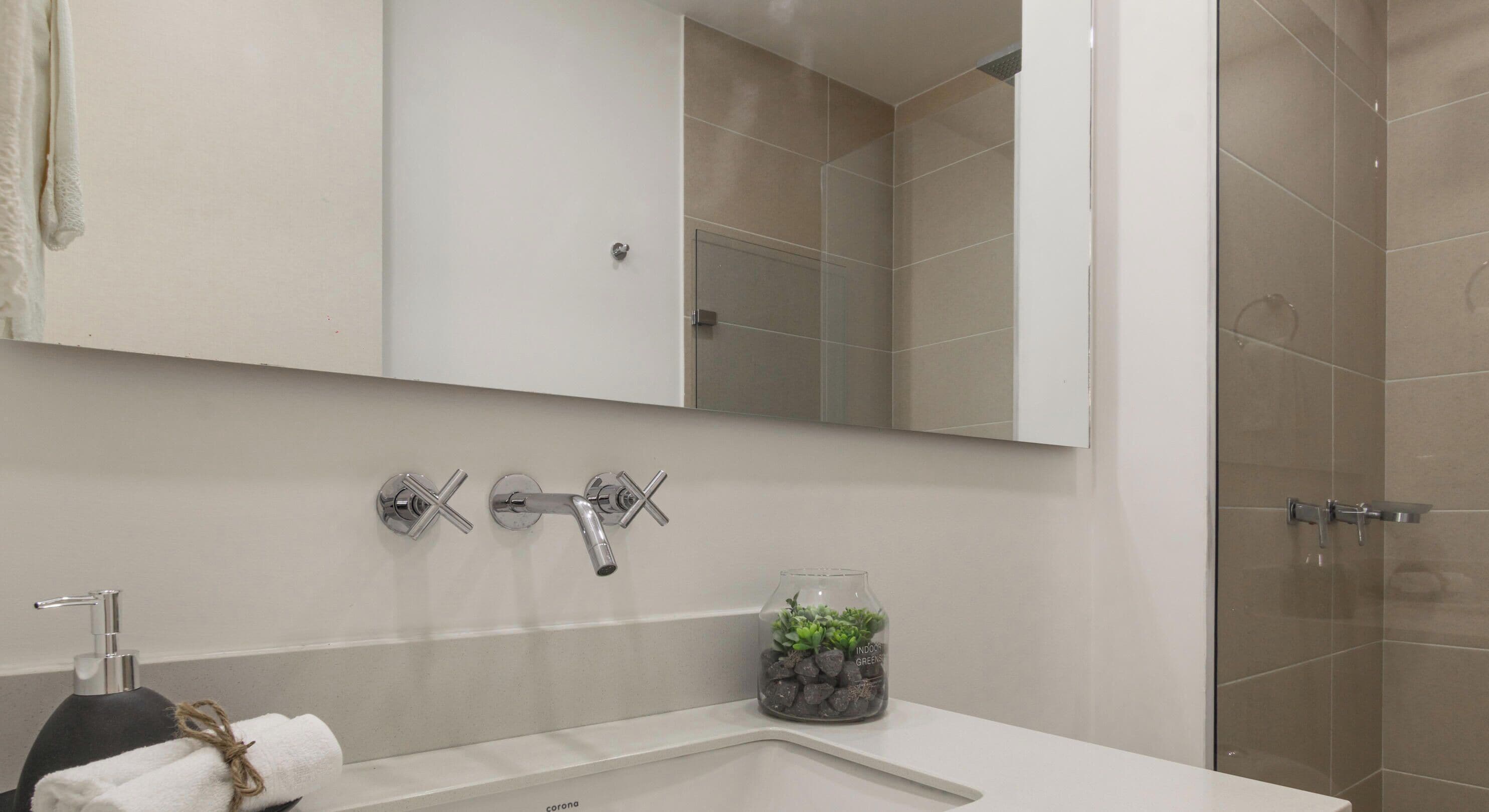 Un baño con lavamanos blanco, un espejo y zona de ducha.