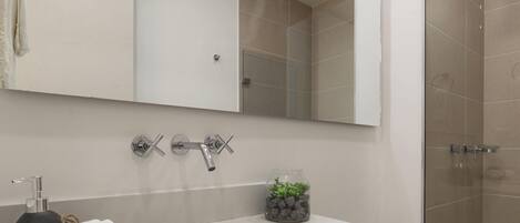 Un baño con lavamanos blanco, un espejo y zona de ducha.