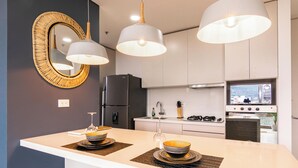 A modern kitchen with a central island, pendant lights, a refrigerator, stove, and a large mirror. - Apartamento Urban Studios (Medellín)